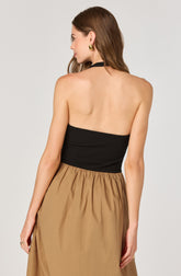 A woman is wearing a black, strapless, halter-style top with a gathered, elastic waistband, paired with a high-waisted, tan-colored skirt that has a gathered, voluminous silhouette. She accessorized with gold earrings and a ring on her left hand.